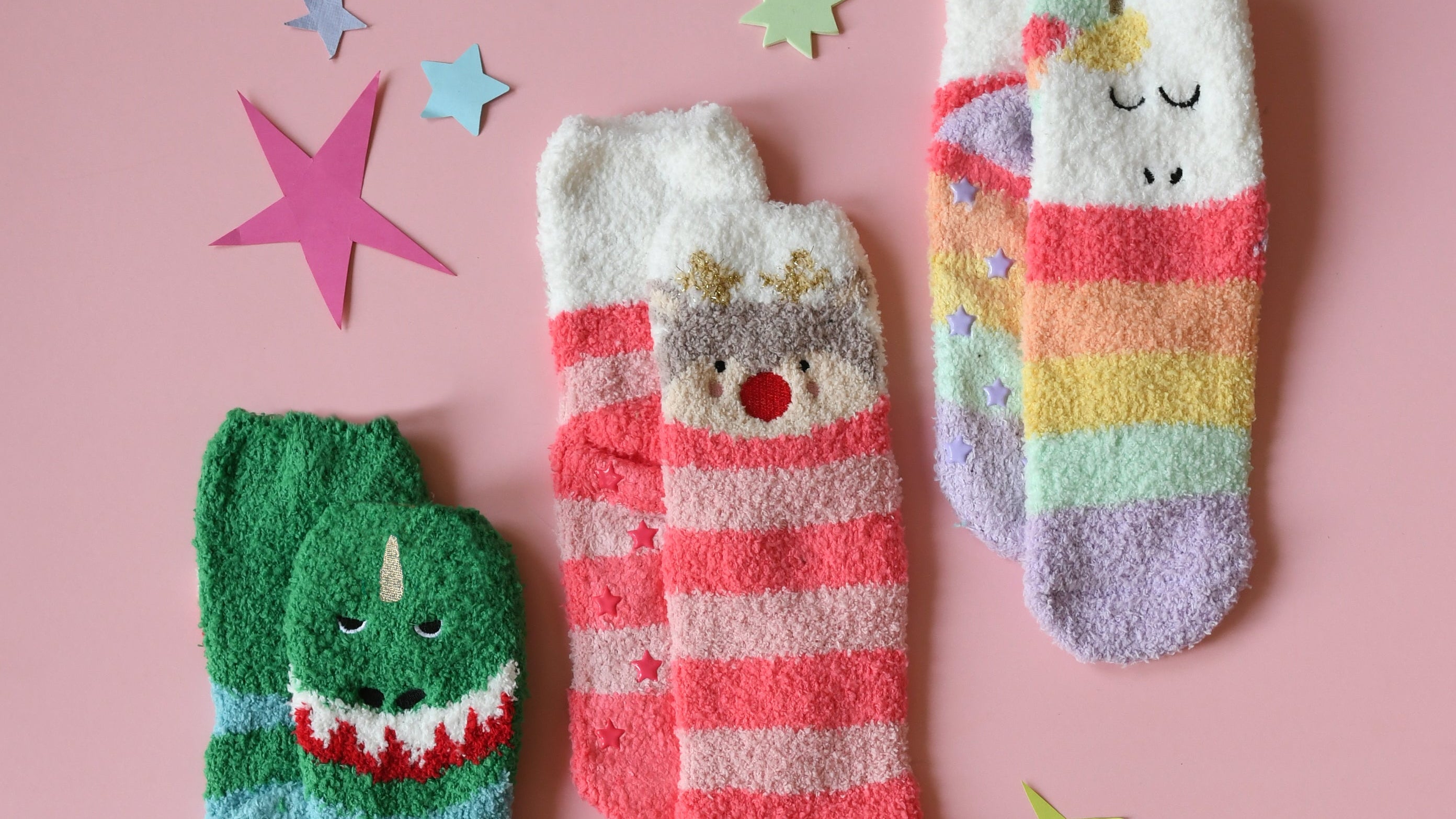 Three pairs of colorful children's socks on a pink background with decorative stars.